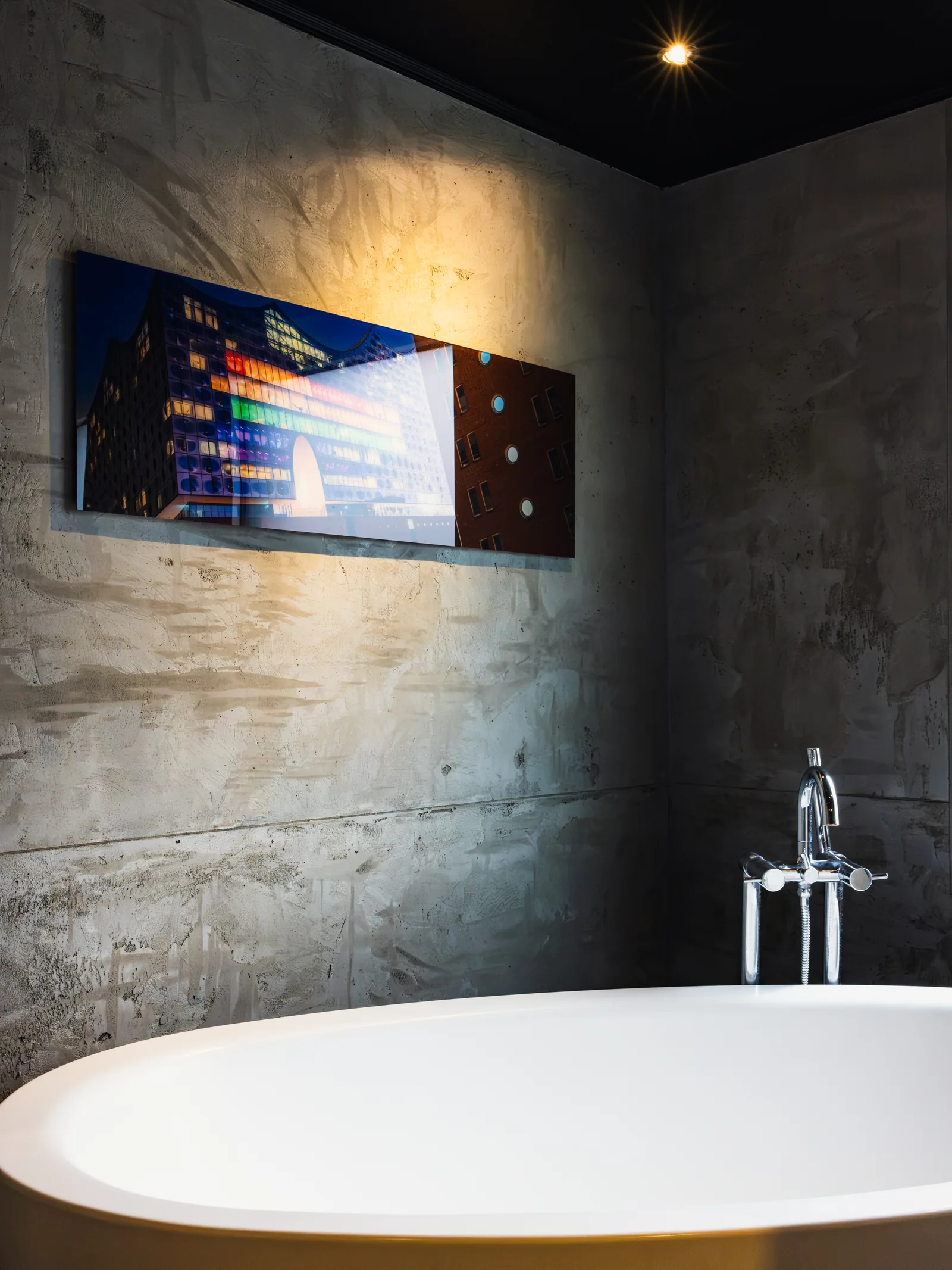 Badezimmer mit Wänden in Betonoptik, freistehender Wanne und beleuchtetem Wandbild